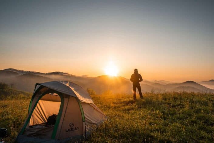 silhouette of man watching sunset near tent