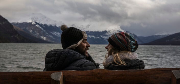 Couple sitting in a wooden bench enjoying the cold weather beside a lake