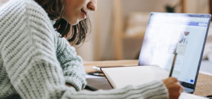 Woman writing on her notebook copying over something from her computer