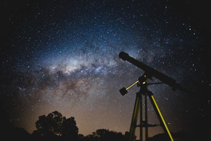 A telescope ready for a magically colored sky full of stars