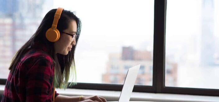 Woman wearing an orange headphone working with her laptop