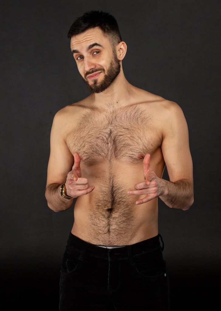 Shirtless muscular man with full and natural chest hair in jeans standing and pointing at the camera