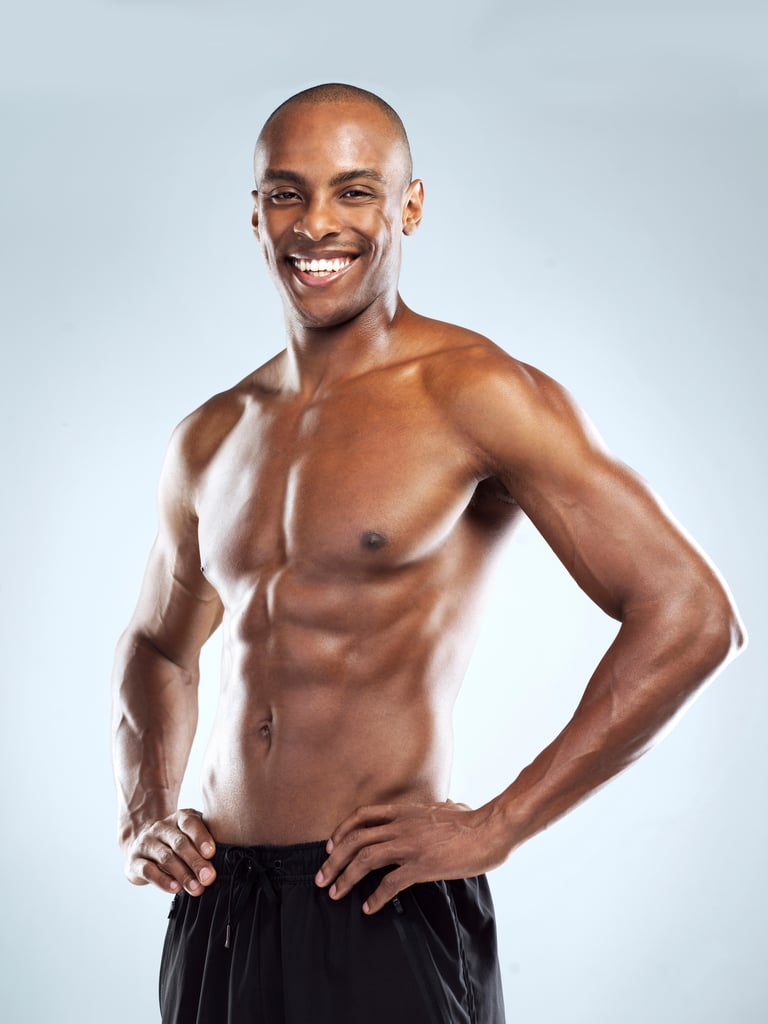 Studio shot of an cheerful athletic young man with clean-shaven chest posing against a grey background.