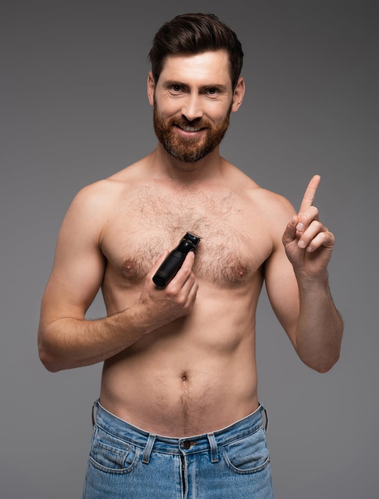 Happy and shirtless man trimming chest hair with electric razor and gesturing isolated on grey background