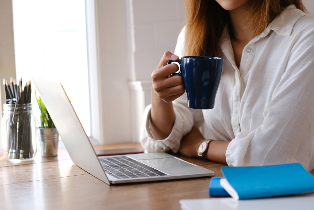 Young woman working on a laptop while holding a coffee cup on a Monday morning, representing focus, energy, on Monday morning.