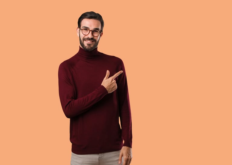 Man in a maroon turtleneck pointing to the side against a solid peach background