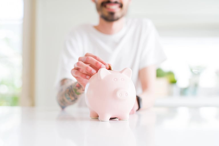 Man placing a coin into a pink piggy bank, representing smart money habits and personal finance savings.