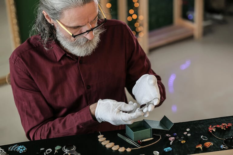 Jewelry designer examining flatback crystals and gemstones on a worktable to create dimension and depth in handcrafted designs.