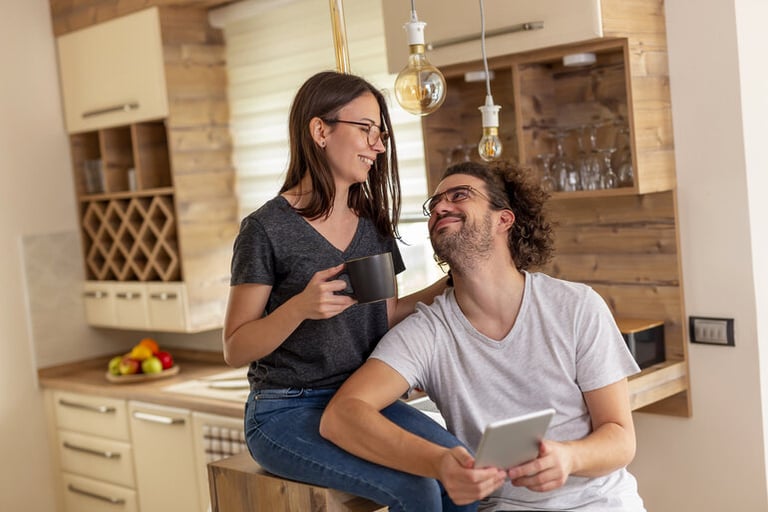 Homeowners relaxing in a modern kitchen while using a tablet, representing comfortable indoor living with a dual-zone ductless AC system.