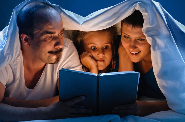 Parents and a child sit together under a blanket, reading a book by soft light, creating a cozy and engaging story night atmosphere.