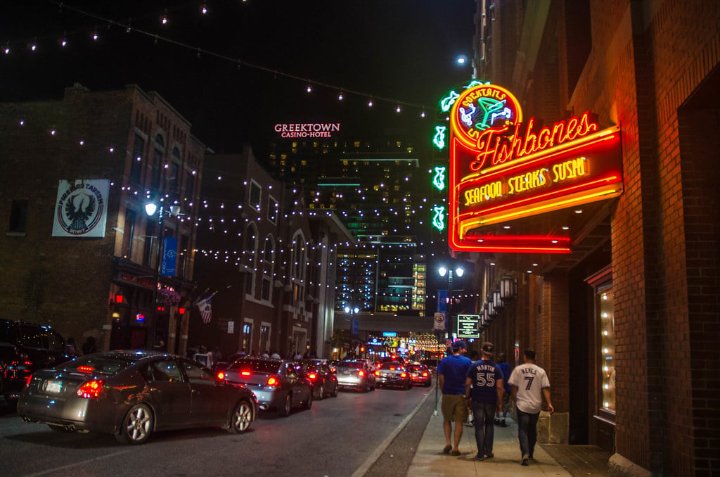 Downtown Greektown Detroit at night, with traffic, men walking, and neon lights.