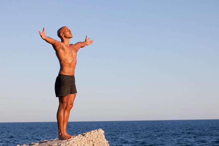 A man is stretching on a rock at a beach.