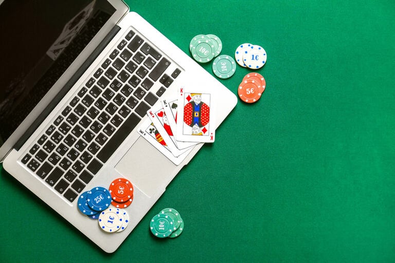 Casino chips and playing cards near a laptop on a green table