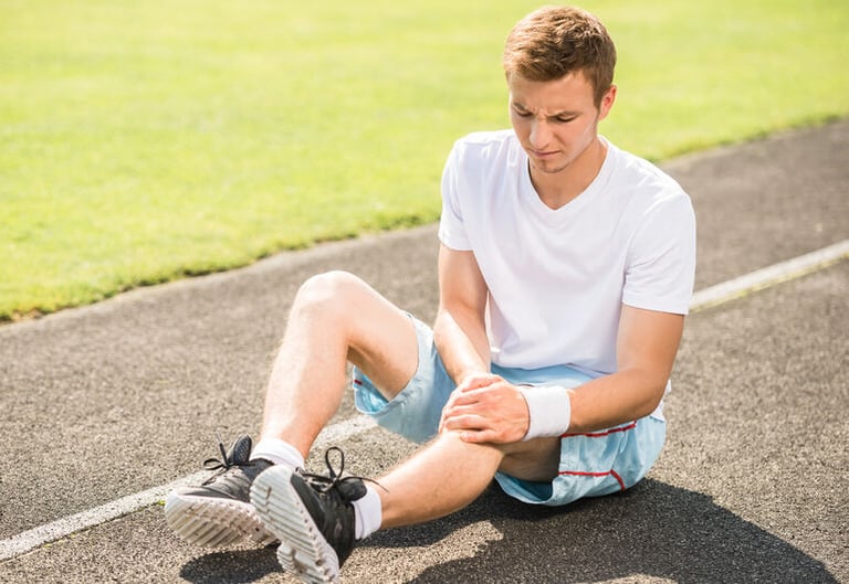 A man sitting on a running track holding his leg in pain after a workout.