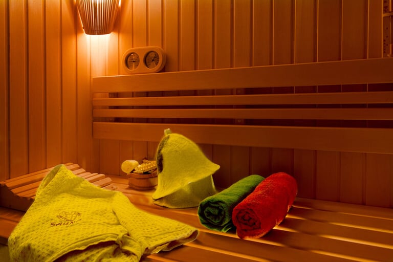 Warm wooden sauna interior with soft lighting, bench seating, folded towels, and a traditional sauna hat for relaxation and stress relief