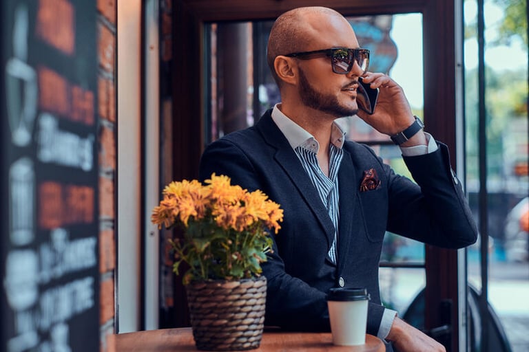 Man in formal attire sitting and using his phone, representing everyday confidence, self-assurance, and authentic personal growth
