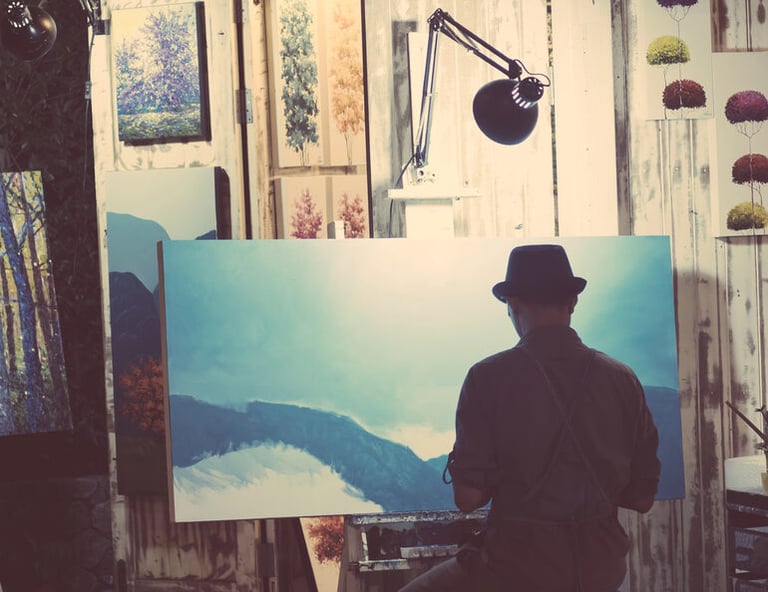 A man in a studio painting a large blue landscape, illustrating a creative pursuit outside of work