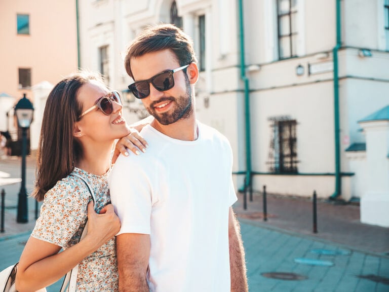 Smiling young couple in sunglasses walking in a sunny city, reflecting modern dating vibes and subtle “beige flag” behaviors