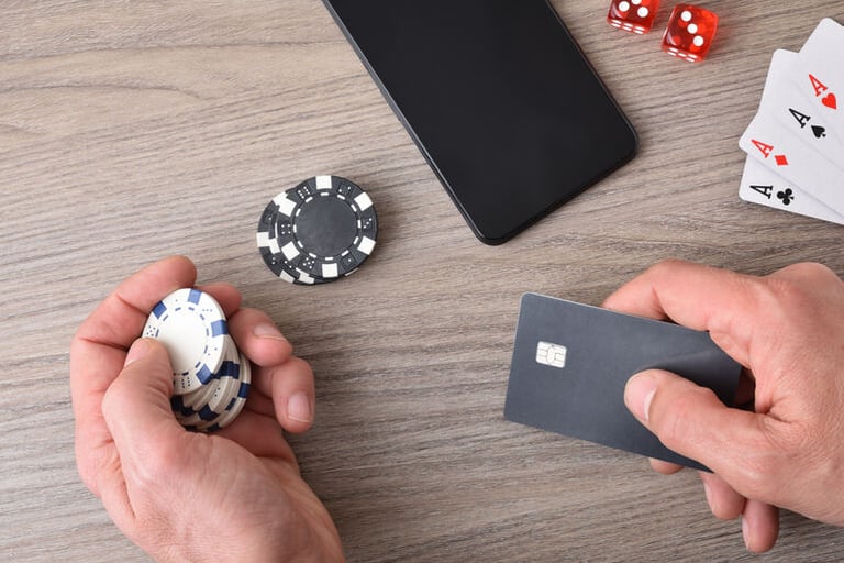 Hand holding casino chips and a card beside a smartphone, showing mobile payments in online gaming