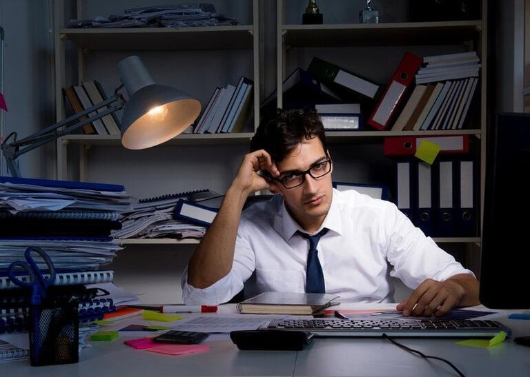 A stressed office worker sitting late at a cluttered desk, overwhelmed by client work and paperwork.