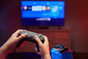 Person playing online games with a controller while viewing a game selection screen on a TV.