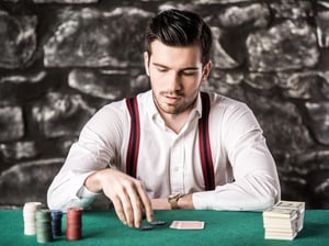 Man sitting at a poker table with playing chips and playing cards, focusing on a game in progress.