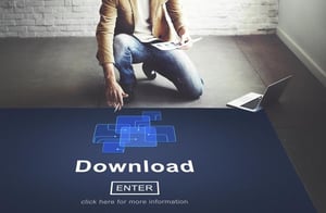 Man kneeling beside a laptop while pointing at a digital “Download” interface on screen, representing proxy servers and online data access.