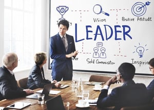 Business professionals in a meeting, as a presenter explains leadership qualities on a whiteboard for a guide on becoming an effective business leader.