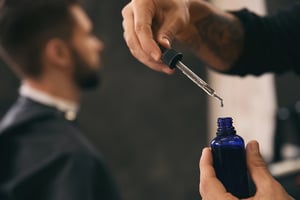 Close-up of a barber using a dropper to apply traditional hair oil to a client’s hair, highlighting grooming care and product use in a salon setting
