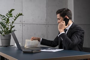 Businessman talking on the phone while reviewing notes at his desk, representing honest success, integrity, responsibility, and professional growth.