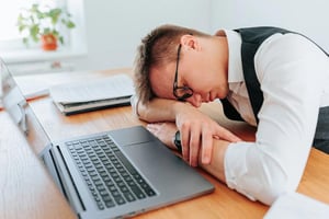 Person feeling tired and losing focus at a desk while working on a laptop, illustrating an afternoon energy and attention slump.