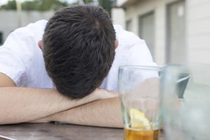 A man sitting alone with his head down beside an unfinished drink, reflecting isolation and the quiet loss of friendships over time.