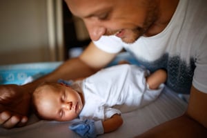 New father caring for sleeping newborn after a difficult birth.