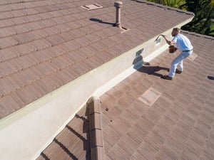 A man applying protective coating to a tiled roof, highlighting durable roofing materials for coastal fog and salt air.