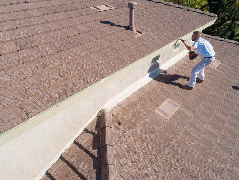 A man applying protective coating to a tiled roof, highlighting durable roofing materials for coastal fog and salt air. 