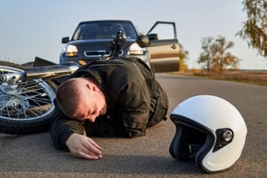 Injured man lying on the road after a motorcycle accident while considering potential settlement compensation.