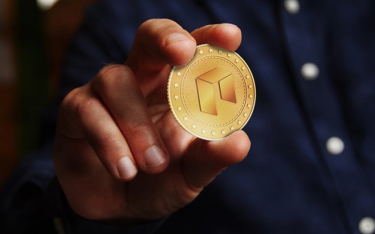 Person holding a gold NEO cryptocurrency coin between their fingers.