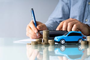 Person reviewing car finance paperwork beside stacks of coins and a model car, representing budgeting for a used car with bad credit.