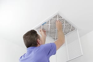A person removing a ceiling air filter.