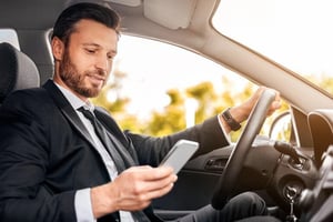 A man sitting happily in a car while checking his crypto wallet on his phone.