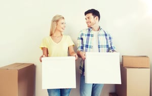 A couple carrying boxes while moving into their new home and preparing to manage a shared household budget.