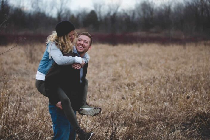 Man carrying his woman while walking through a field.