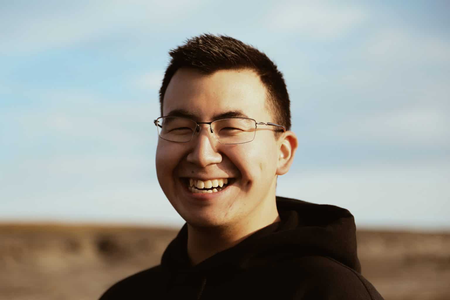 A smiling cheeky eyed man wearing glasses and hoodie