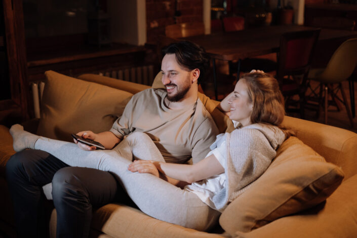 Couple cuddling on a couch while watching TV.