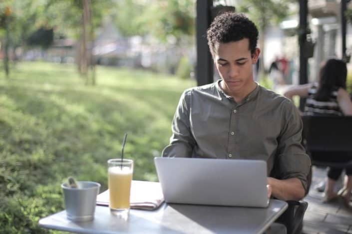 Focused black male freelancer using laptop in street cafe