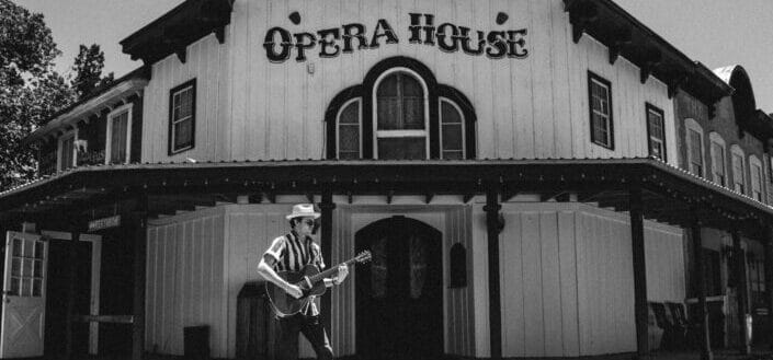 Man playing a guitar in front of an Opera House