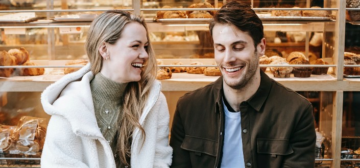 a woman looking at a smiling man inside a bakery