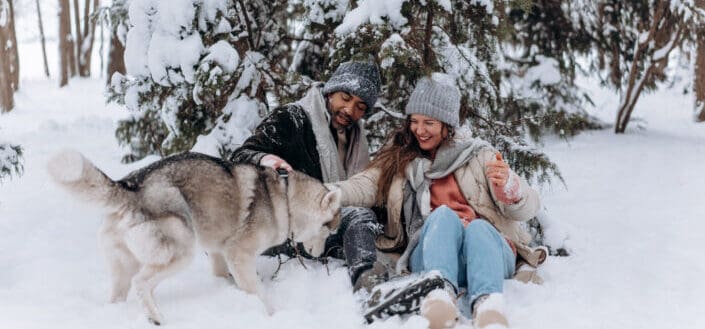 two people playing with a dog in the snow