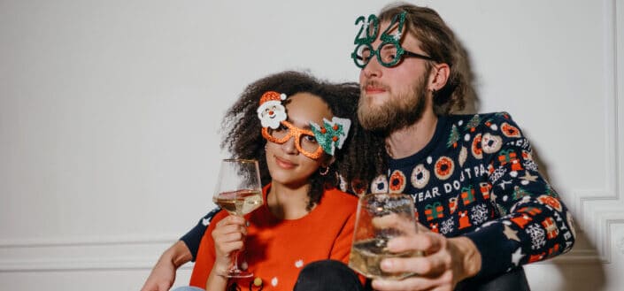 man and woman sitting closely while wearing festive outfits and statement eyeglasses