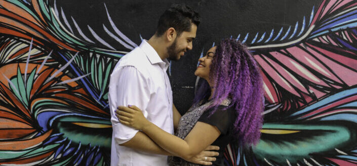 man and woman holding each other's arms with a colorful wall background